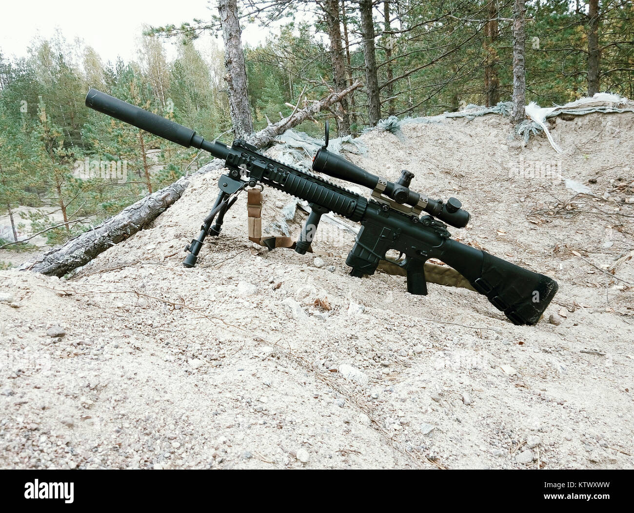 Assault rifle on the background of pine forests and sand. Stock Photo