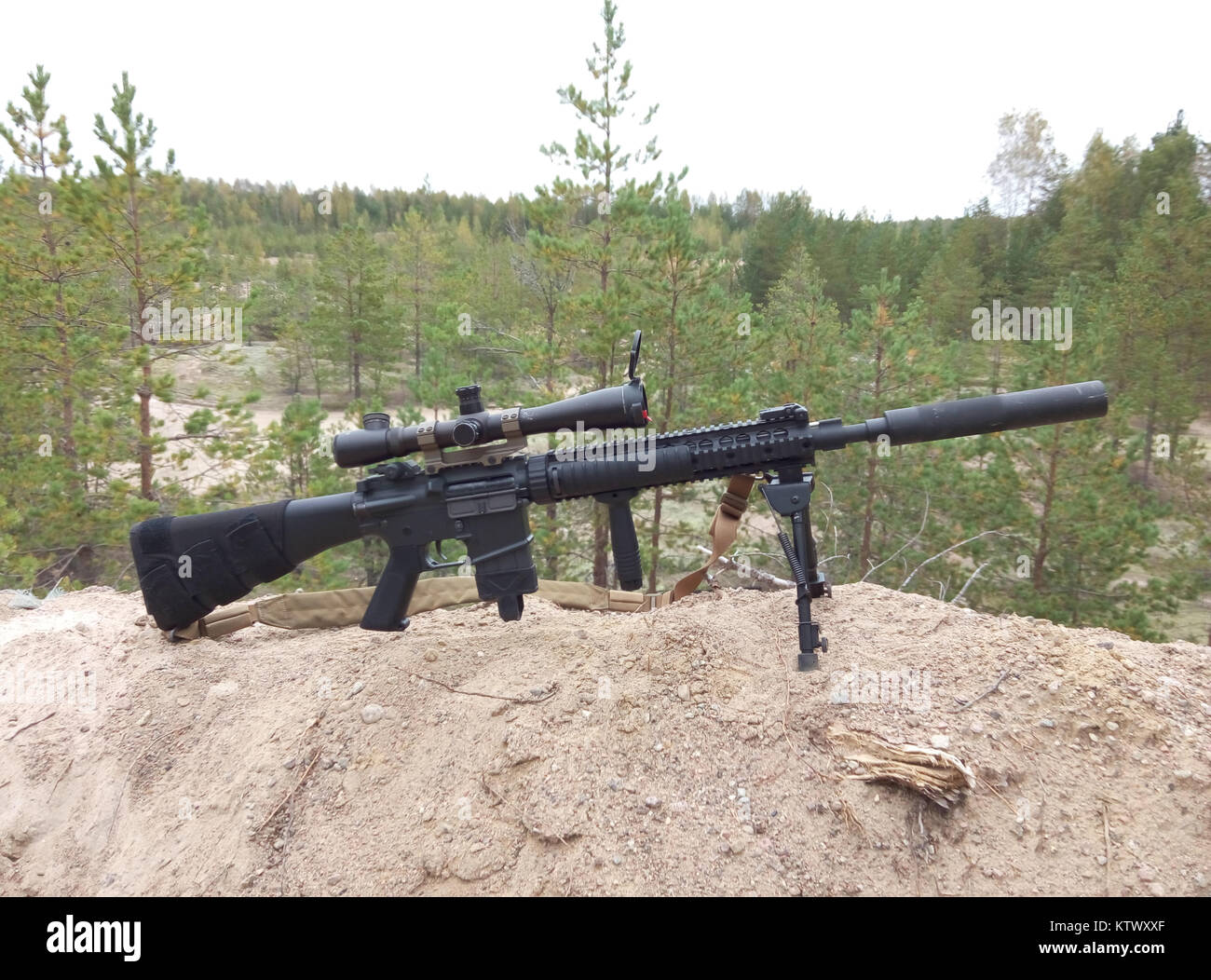 Assault rifle on the background of pine forests and sand. Stock Photo
