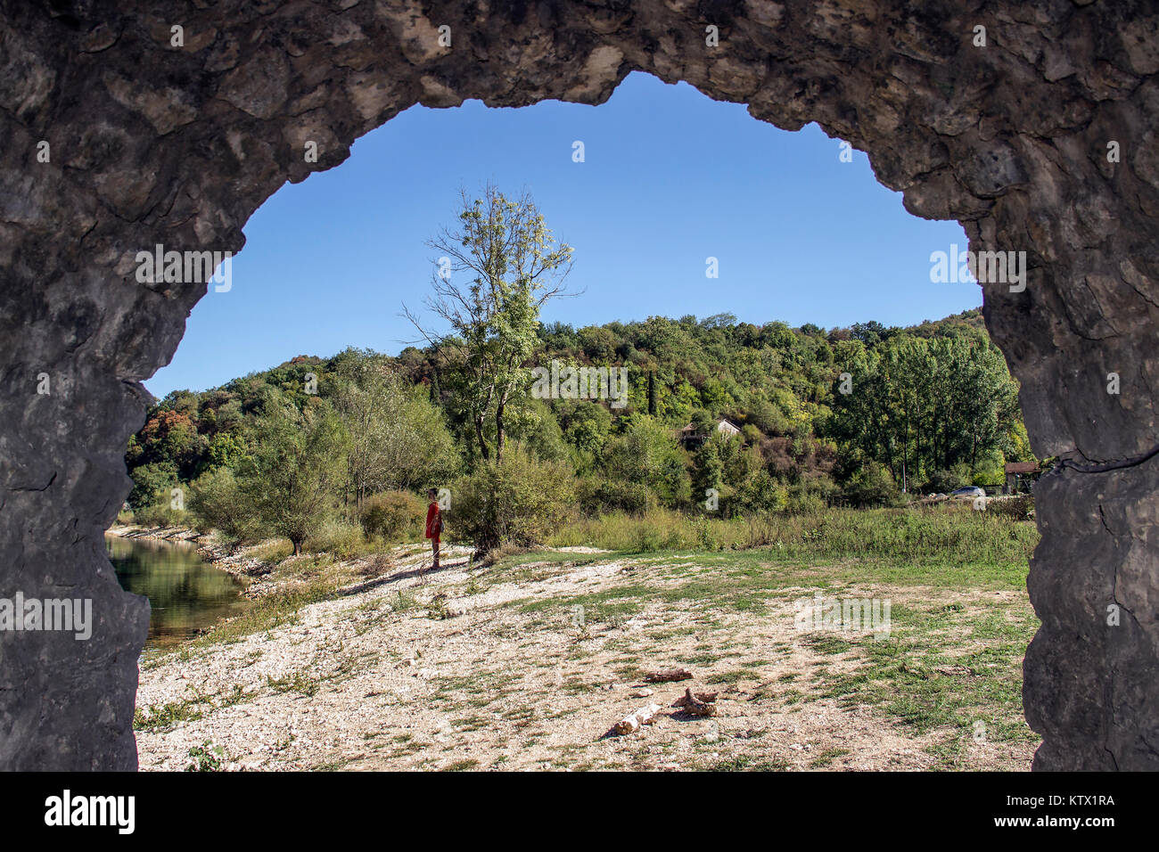 Rijeka Crnojevica, Montenegro - View through the arch of an old stone bridge of a woman observing the river bank Stock Photo