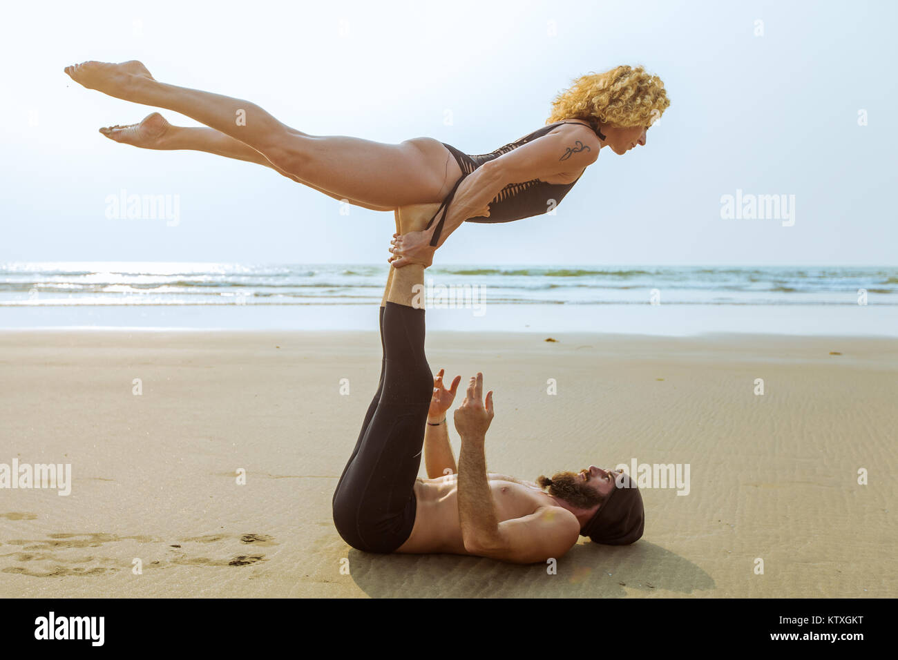 Couple of beautiful people practicing acro yoga on the beach at sunset in Goa, India Stock Photo