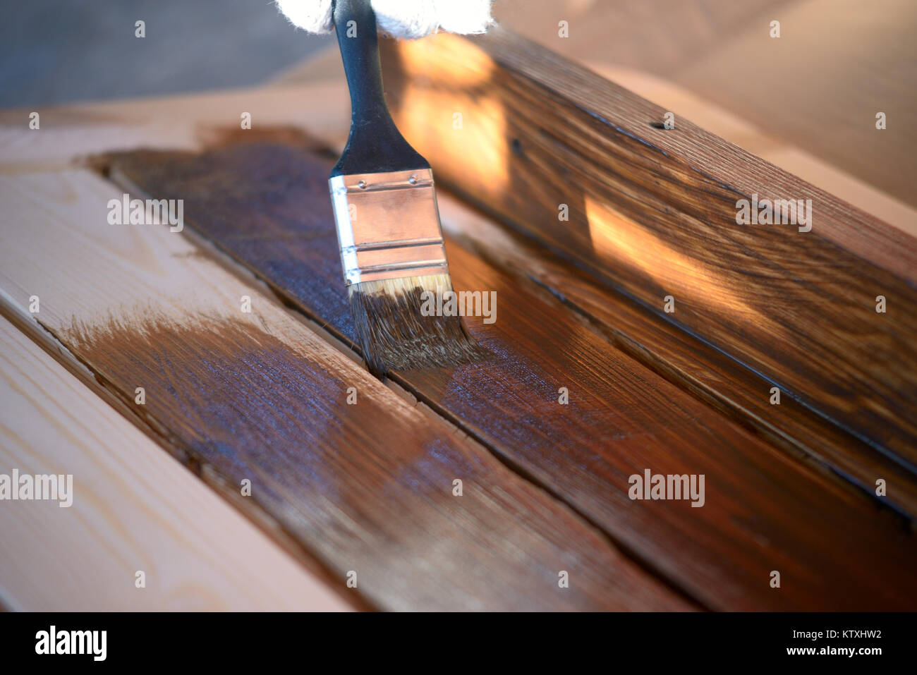 Hand with a brush paints a wooden surface with brown paint, close up Stock Photo