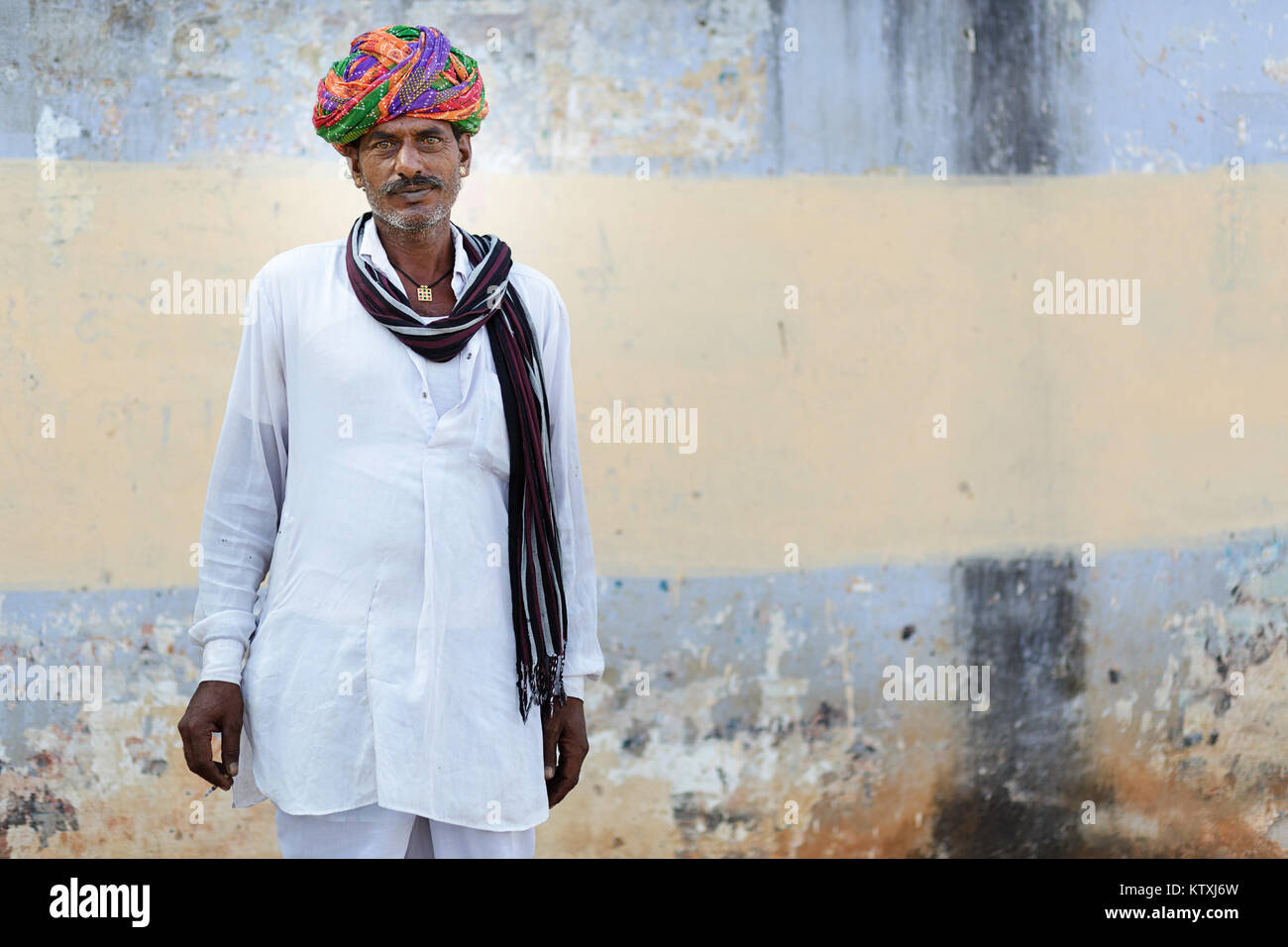 Portrait of old indian man with mustache, green eyes in white outfit with a colorful turban and a scarf, in a village near Pushkar, Rajasthan, India. Stock Photo
