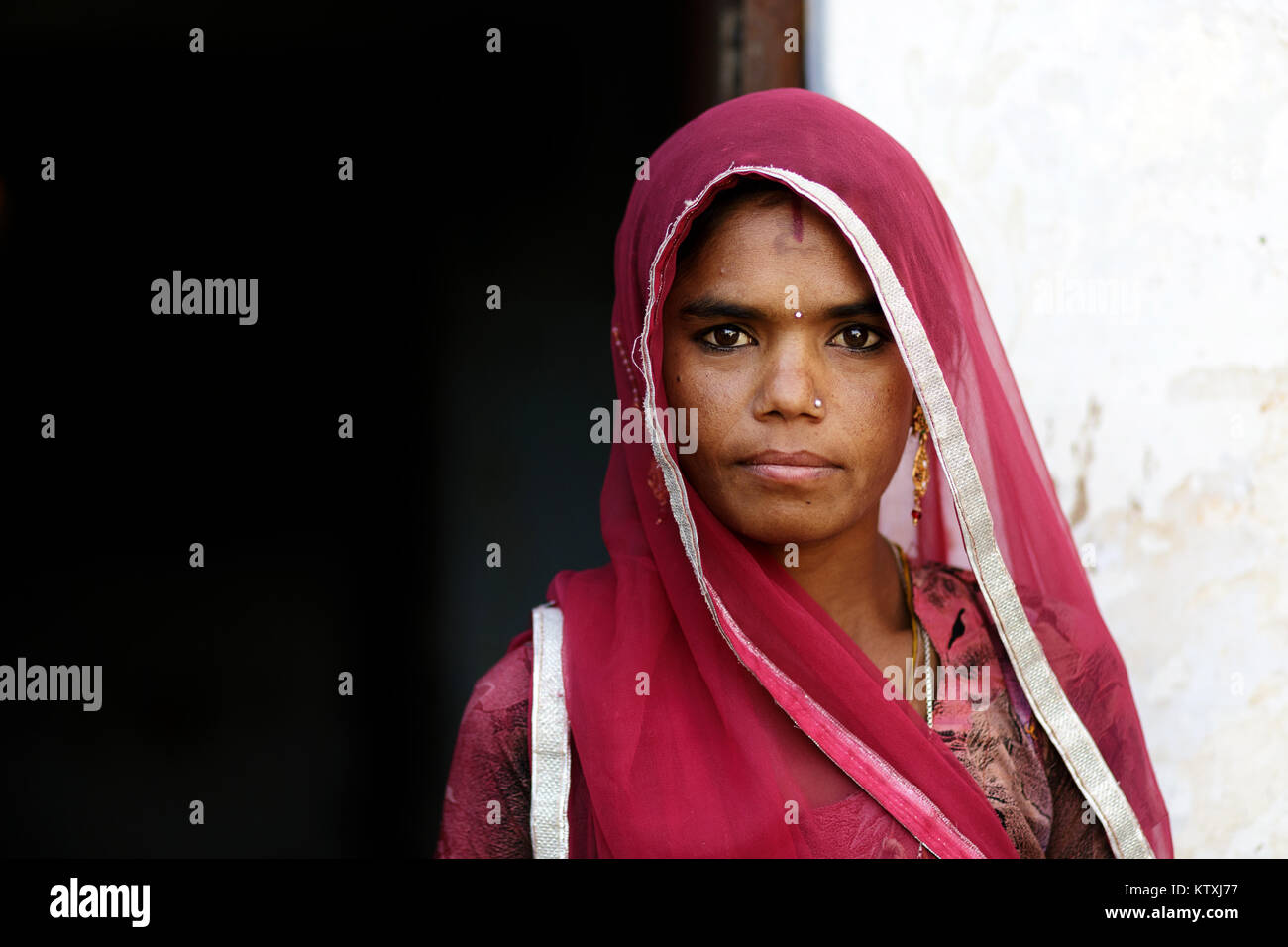 Portrait of young indian woman wearing sari and a veil over her hair in her home, village near Pushkar, Rajasthan, India. Stock Photo