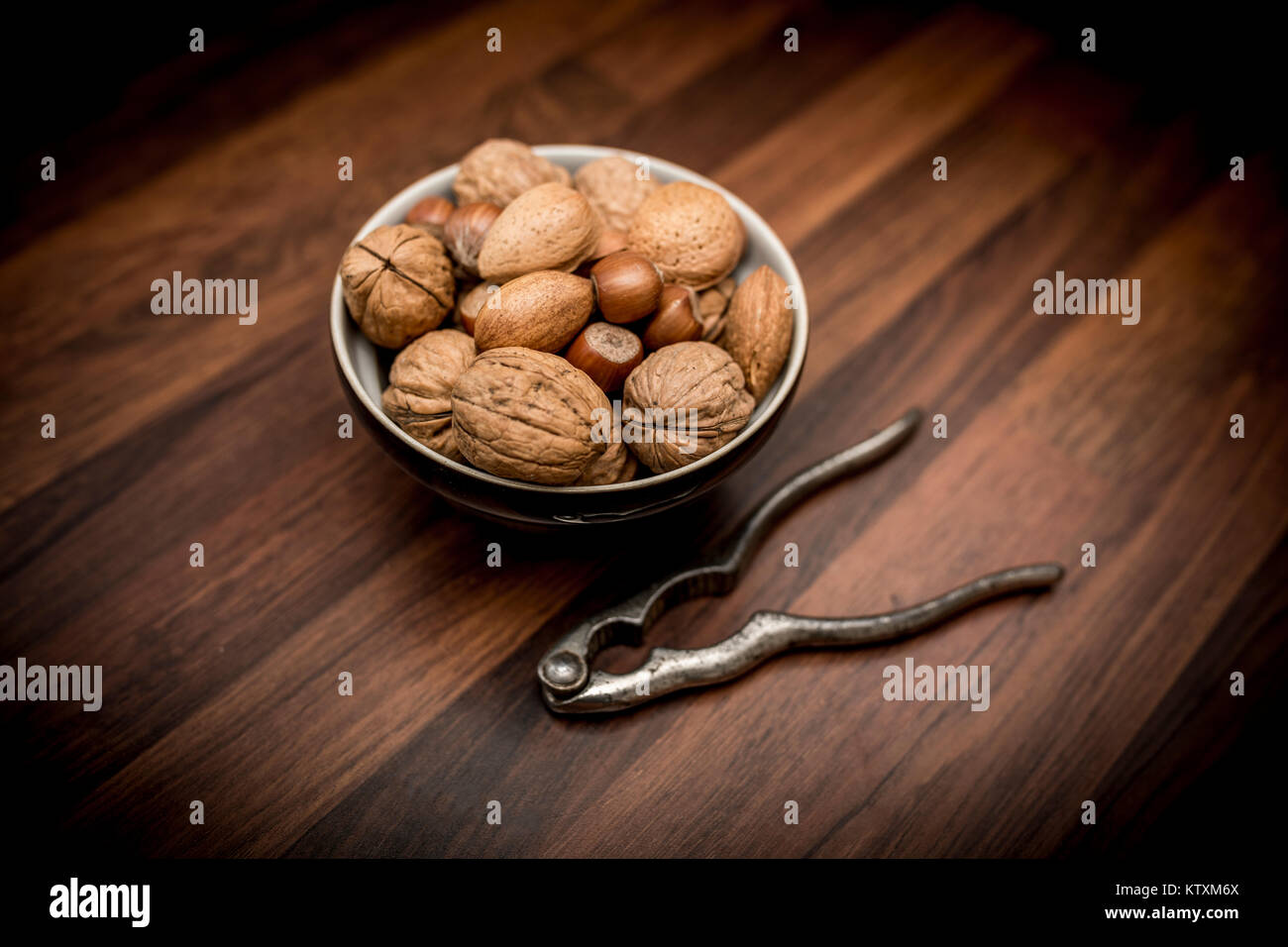 A bowl of mixed whole nuts in their shells including walnuts, hazelnuts, almonds and pecans with nut cracker Stock Photo