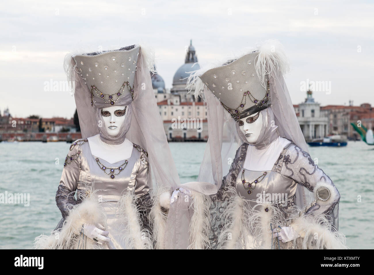 Venice Carnival 2017, Veneto, Italy two women in silver  posing at the lagoon with Basilica Santa maria della Salute behind Stock Photo