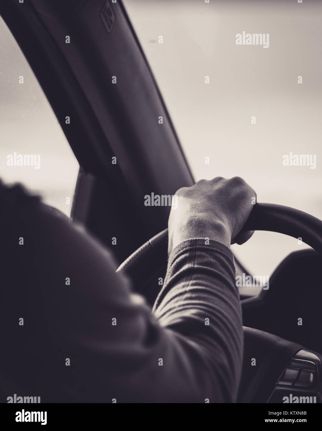 Person with hand on steering wheel driving down the highway, in black and white Stock Photo