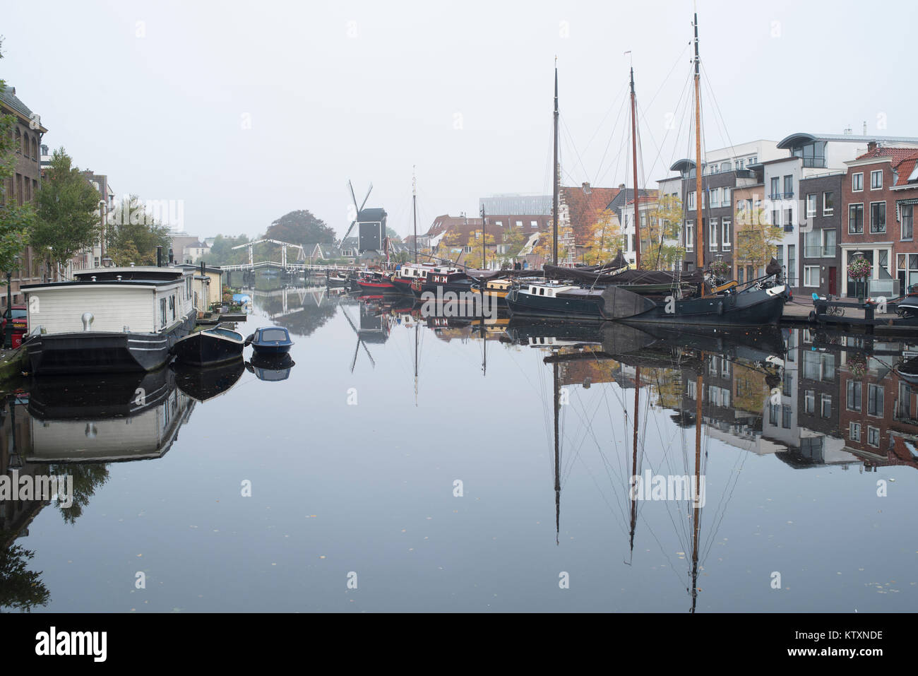 Ships, Windmill and Houses are reflected in a canal on a foggy morning in Leiden, Netherlands Stock Photo