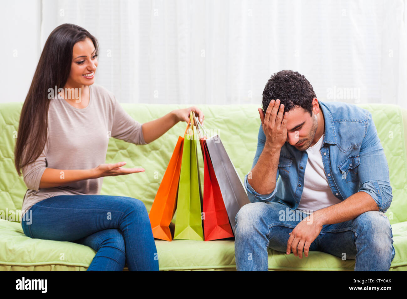 Young couple is sitting at sofa at home. Man is getting bored of talking about shopping. Stock Photo