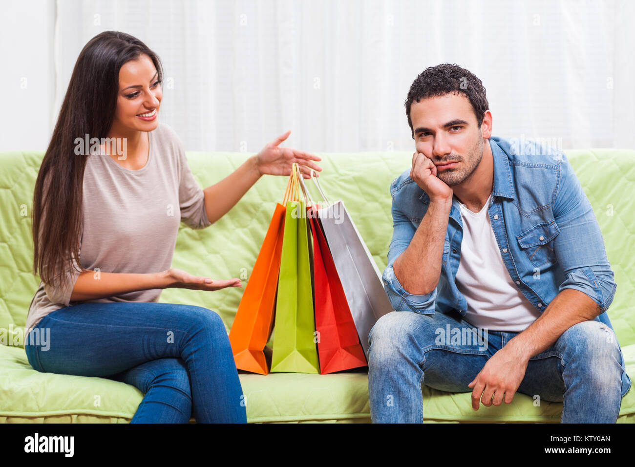 Young couple is sitting at sofa at home. Man is getting bored of talking about shopping. Stock Photo