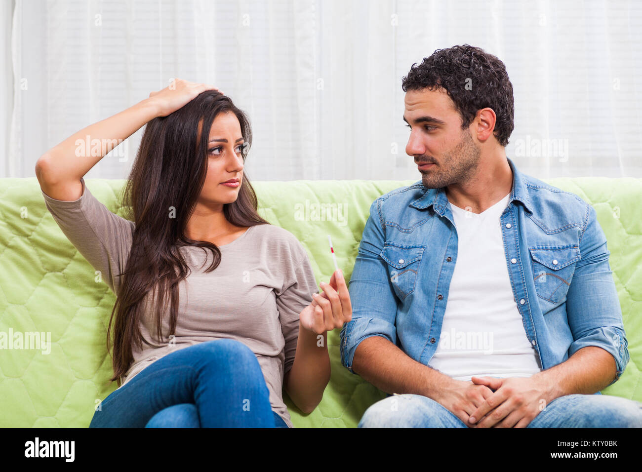 Young couple is looking at positive pregnancy test. They are upset and worried. Stock Photo