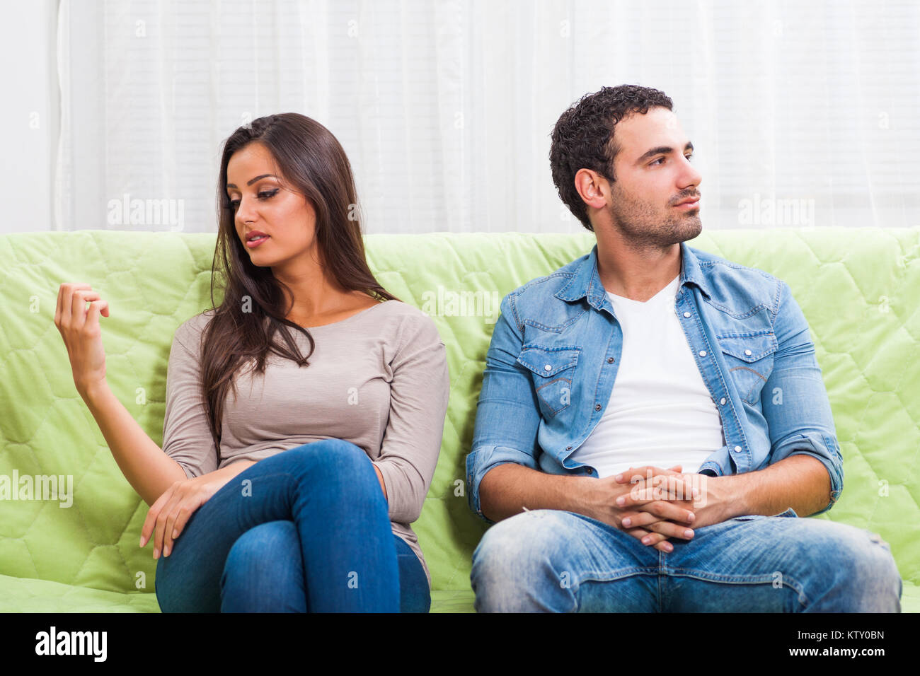 Young couple is sitting on sofa at home and they are getting bored. Stock Photo