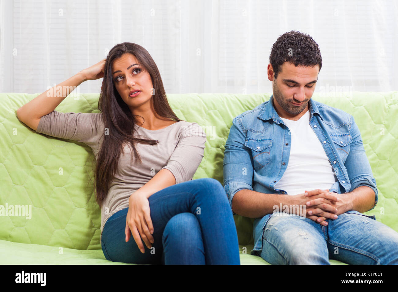 Young couple is sitting on sofa at home and they are getting bored. Stock Photo