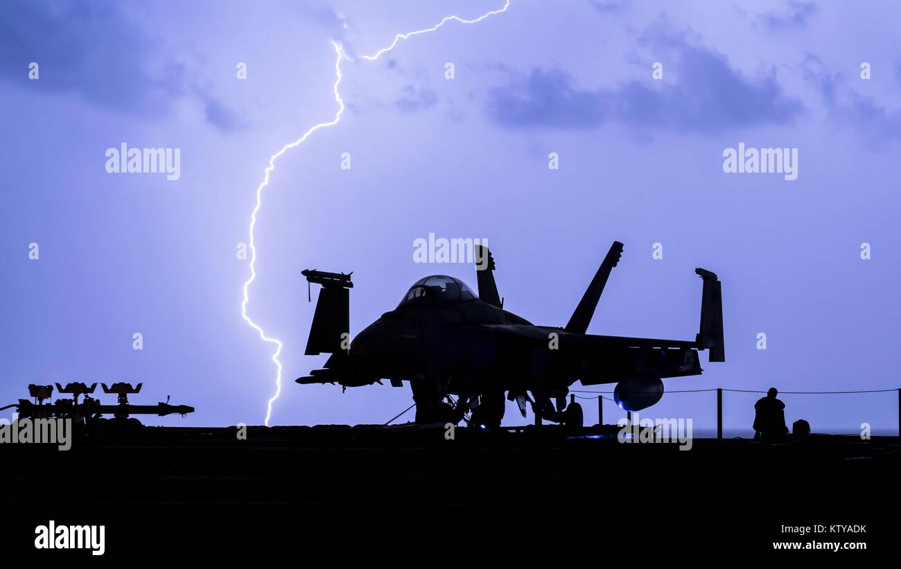 Lightning strikes in the sky behind an aircraft on the flight deck of the U.S. Navy Nimitz-class aircraft carrier USS Theodore Roosevelt December 16, 2017 in the Persian Gulf. Stock Photo