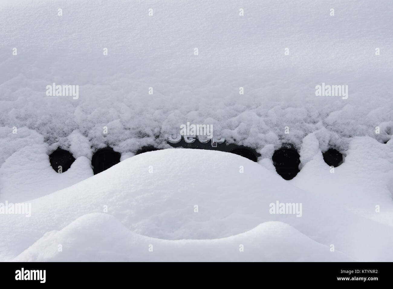 The front of a black Jeep Wrangler covered in snow with just the chrome Jeep emblem visible. Stock Photo