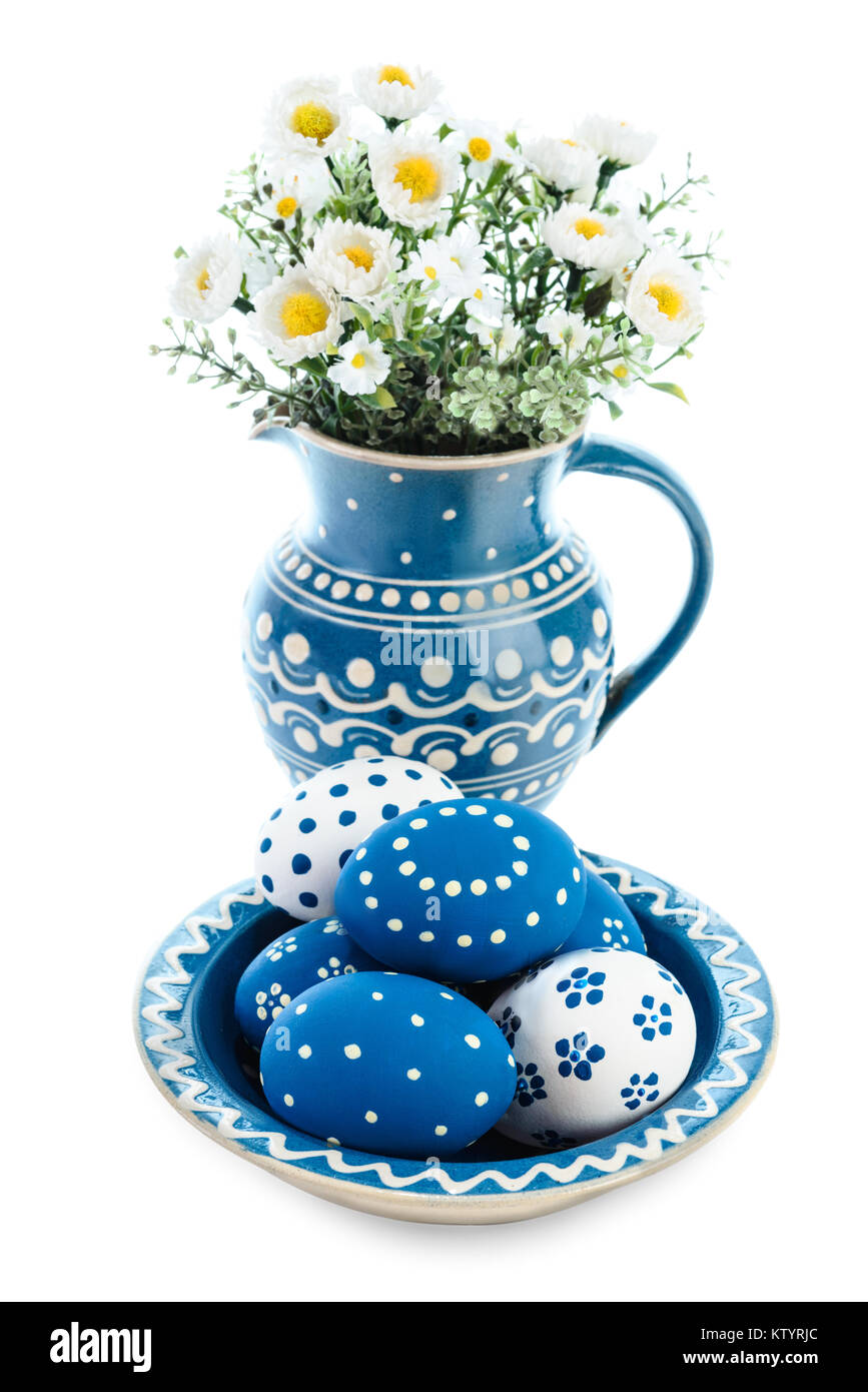 Blue ceramic plate with painted Easter Eggs and flowers in matching vase on white background Stock Photo