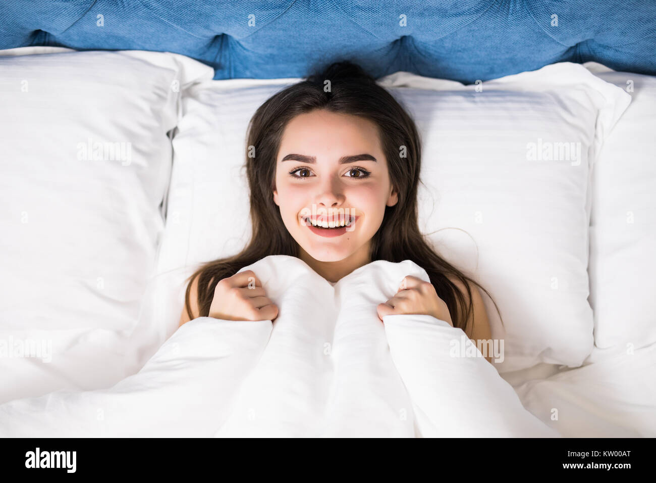 Girl hides her face in bed. Cheerful girl in bed hiding her face under
