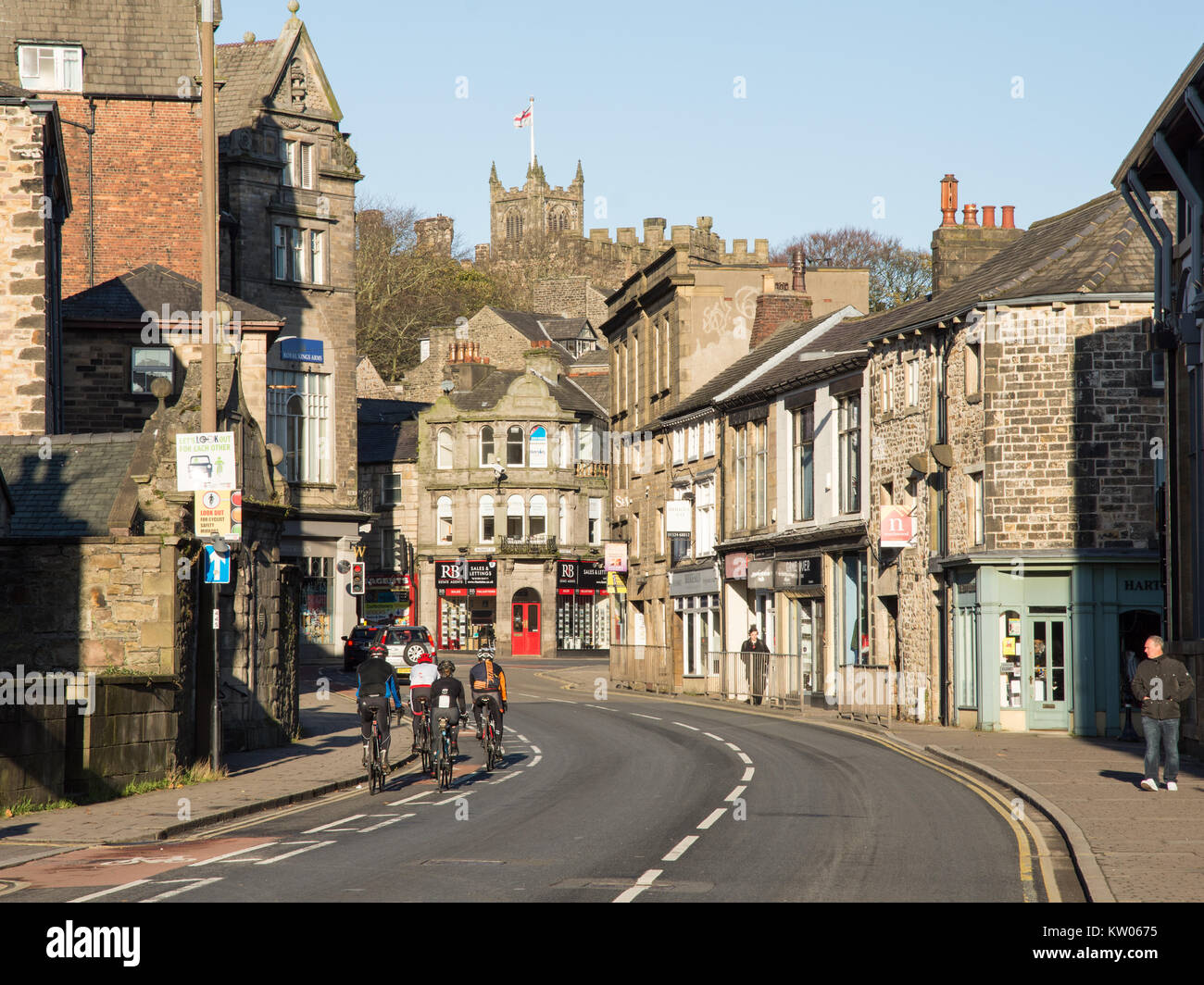Lancaster, England, UK - November 12, 2017: A group of road cyclists ride past shops and houses on King Street in Lancaster, under the towers of Lanca Stock Photo