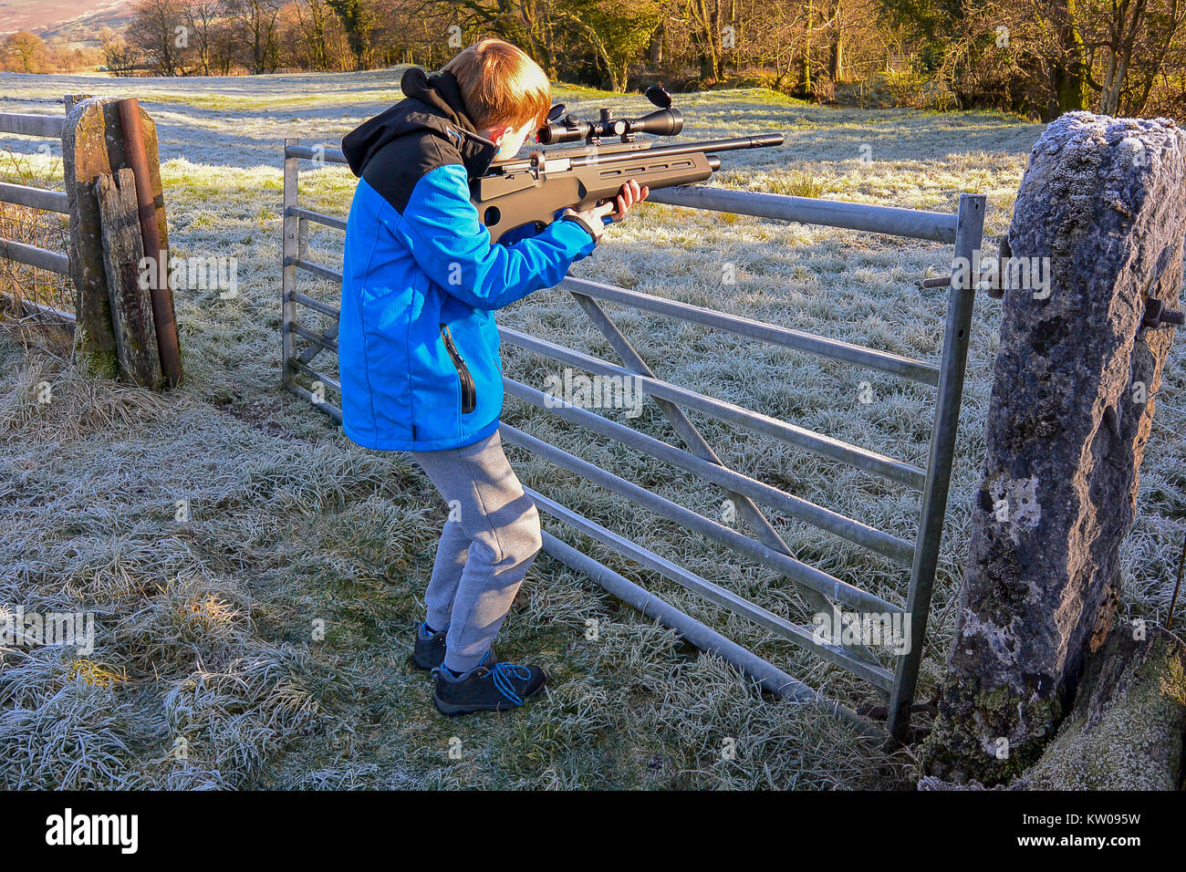 Teenage boy firing an air rifle on farmland on a cold, frosty day Stock Photo