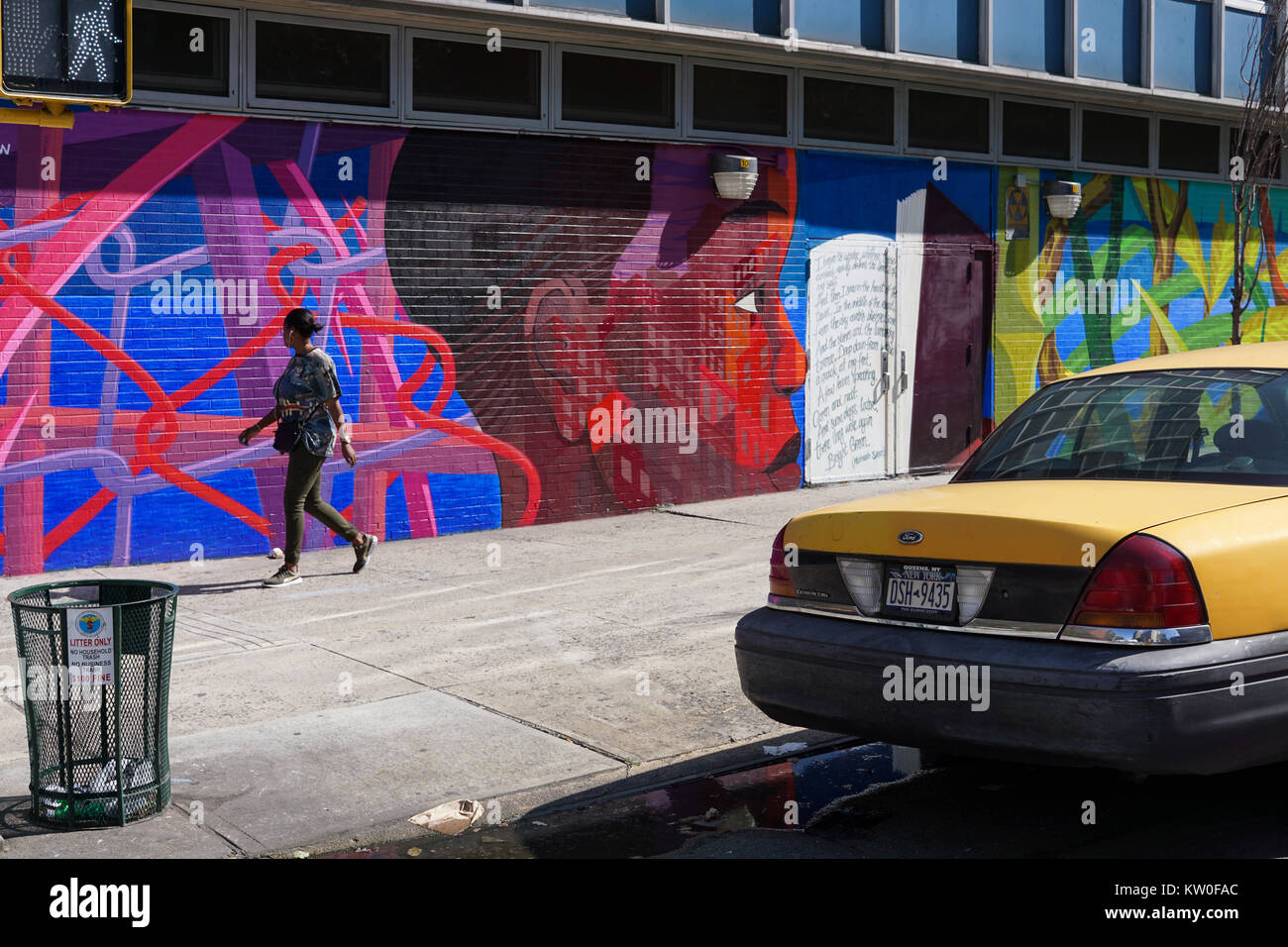 A girl walks past a wall with street art in East Harlem on a sunny afternoon. Stock Photo