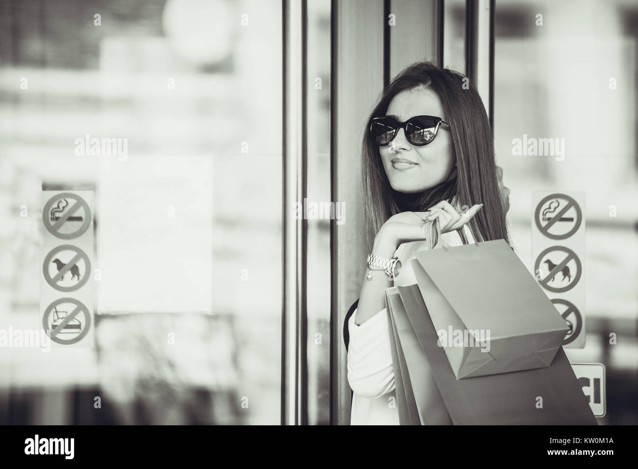 Beautiful happy girl in sunglasses is holding shopping bags, looking at ...