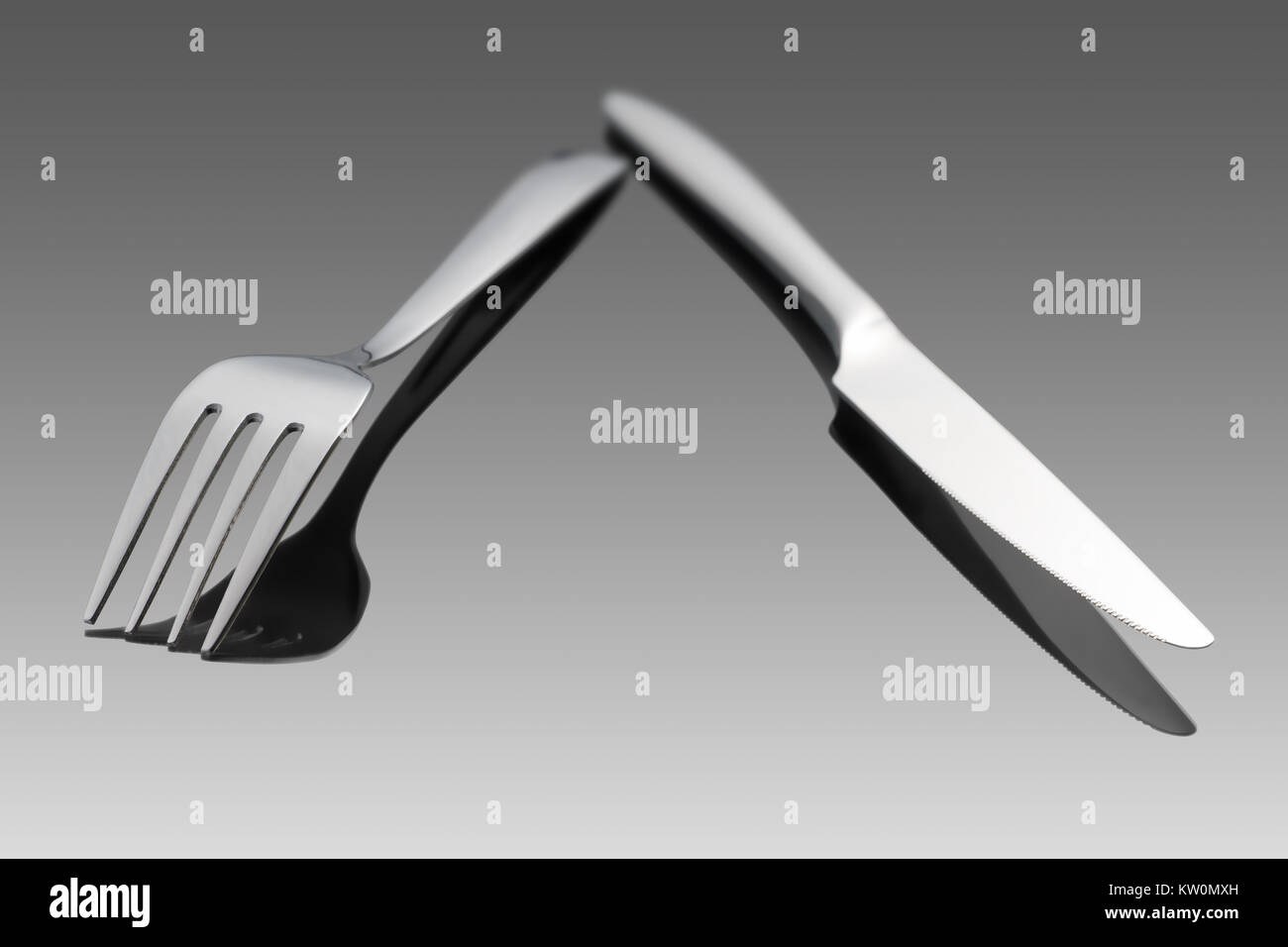 Fork and knife laying on gray gradient background with reflection. Selective focus Stock Photo
