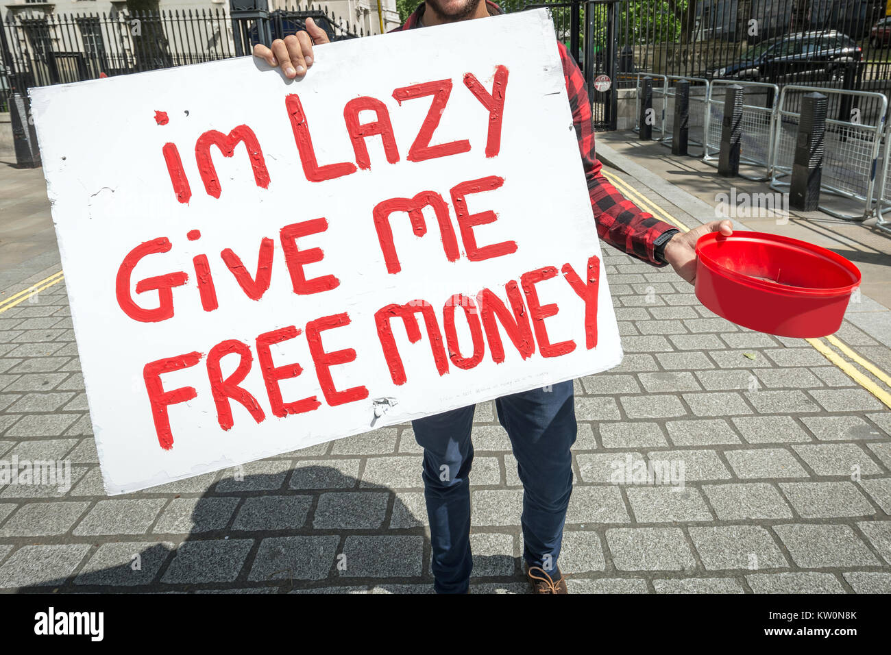 A young student protester holds a begging bowl and humorous placard 'I'm lazy give me free money' on Whitehall in London, UK. Stock Photo