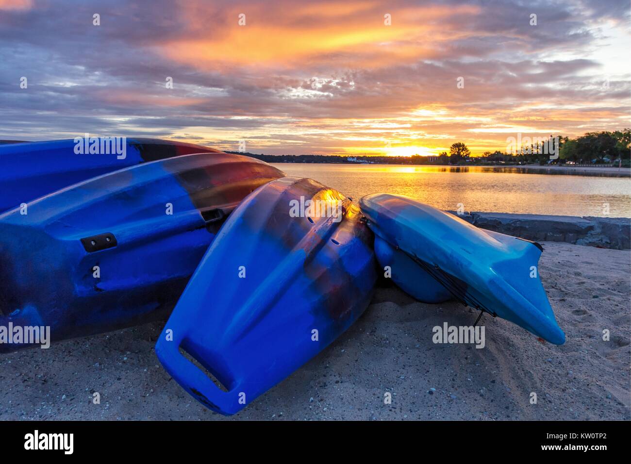 Summer Kayak Sunrise. Row of colorful Kayaks line the shore of a sandy beach as sunrise colors reflect in the calm waters of Lake Michigan. Stock Photo