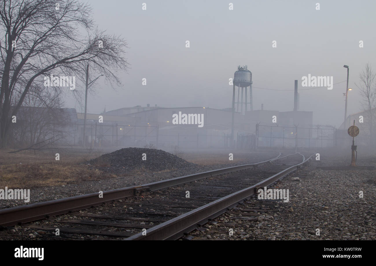 Train tracks lead to a factory warehouse and water tower as downtown Port Huron is enveloped in a thick fog. Port Huron, Michigan Stock Photo