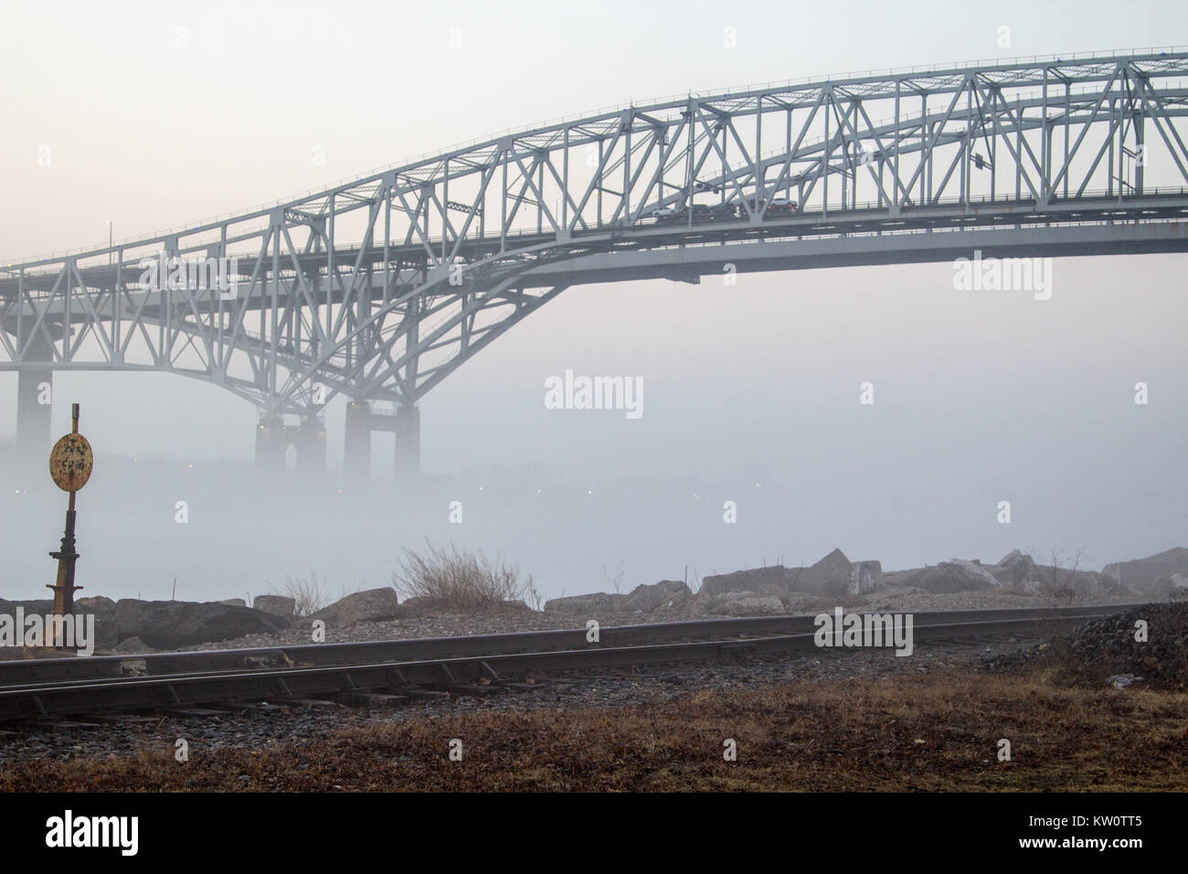 The International Blue Water Bridge in heavy fog with railroad tracks in the foreground. The Blue Water Bridges connects the USA and Ontario, Canada. Stock Photo