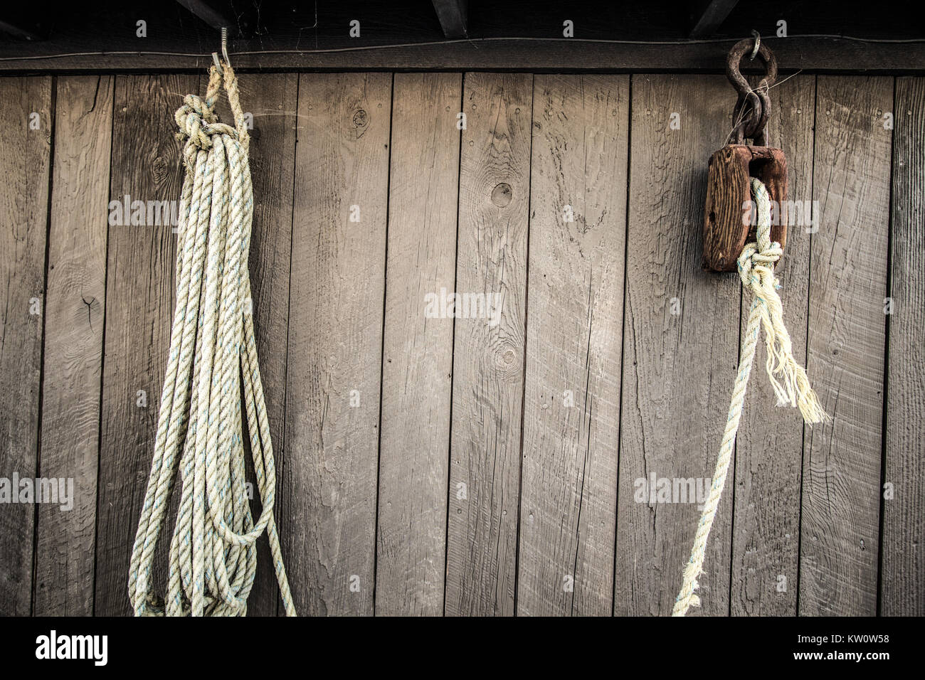 Block And Tackle Pulley. Fisherman's block and tackle pulley system with white rope set against a weathered wooden background. Stock Photo