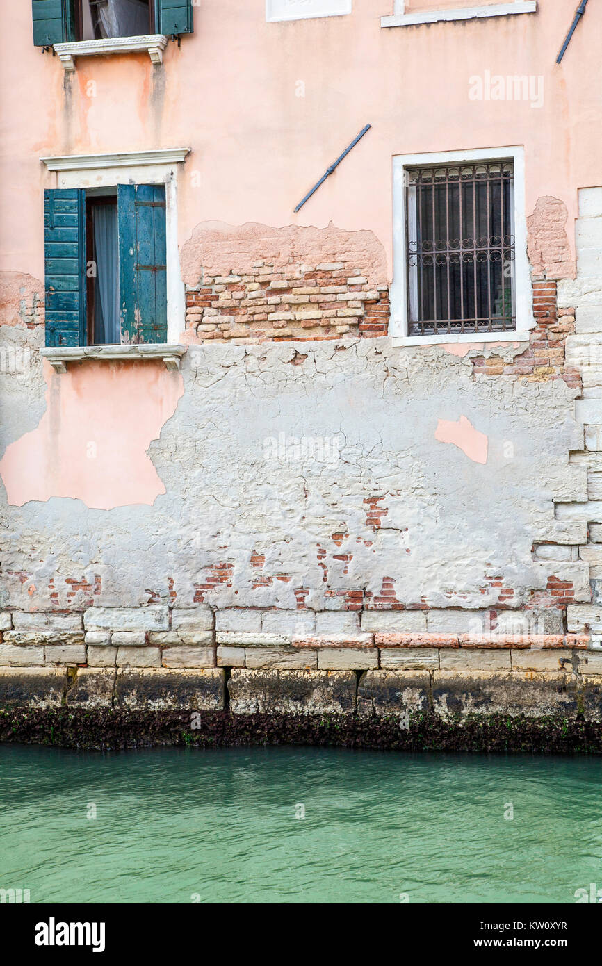 Side of a Venice building on a canal with crumbling brickwork and rendering and shuttered windows Stock Photo