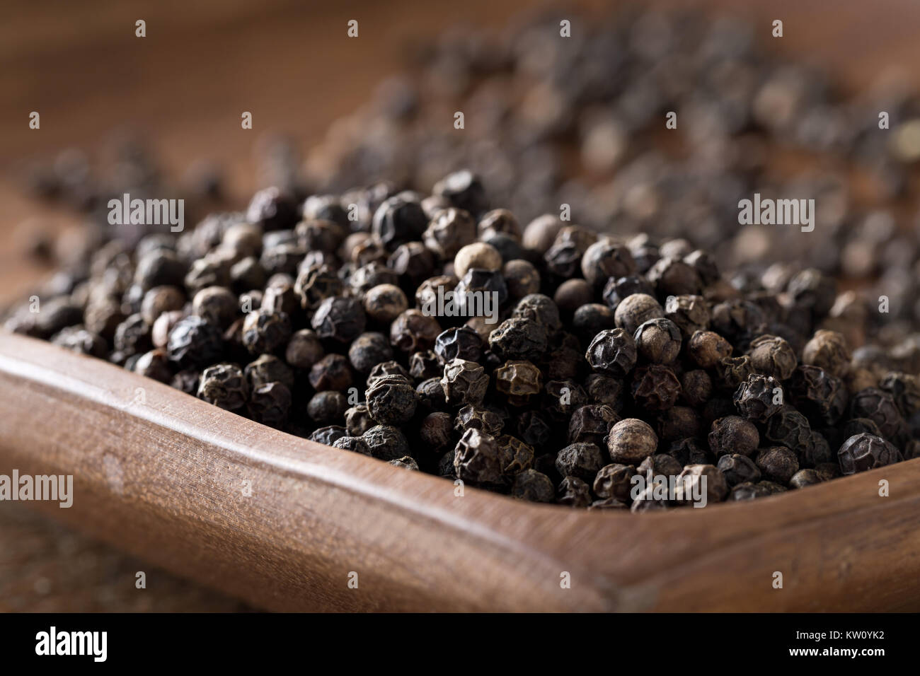 Raw, natural, unprocessed black pepper peppercorns on wooden plate with selective focus Stock Photo