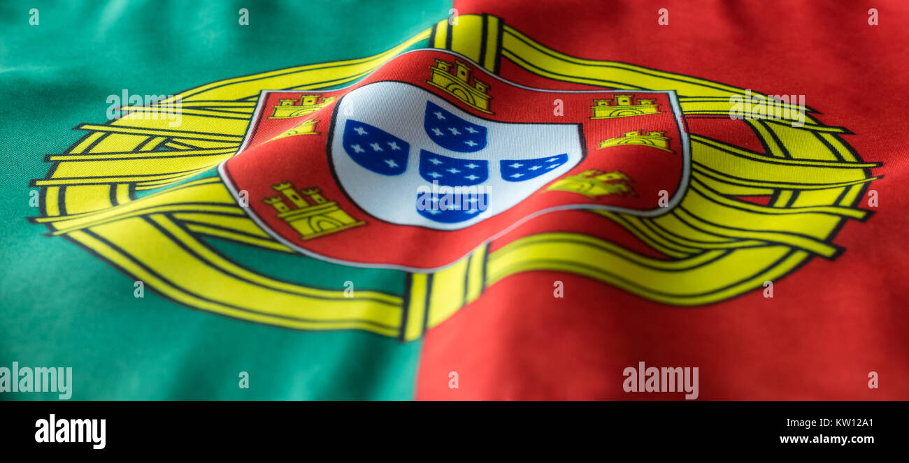 A Portuguese flag is seemingly waving in the wind. The Coat of Arms in between the bold red and green colors is a great symbol for the country of Port Stock Photo