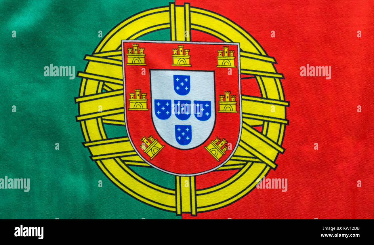 A Portuguese flag is pictured as it lays on a flat surface. The Coat of Arms in between the bold red and green colors is a great symbol for the countr Stock Photo
