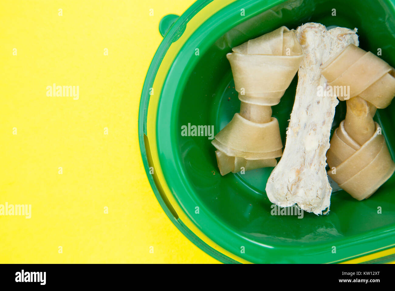 Pet food concept. Delicious snacks for your pet. A green plastic bucket with chewing bones for your dog. Close up. Yellow one-color background. Stock Photo