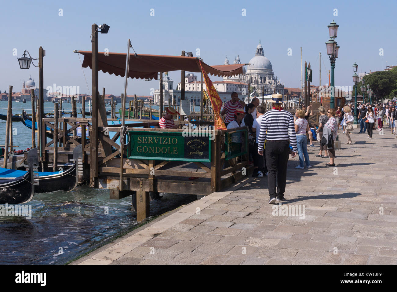Gondoliers wearing traditional costumes at a Servizio Gondole with the Punta della Dogana in the background, Venice Stock Photo