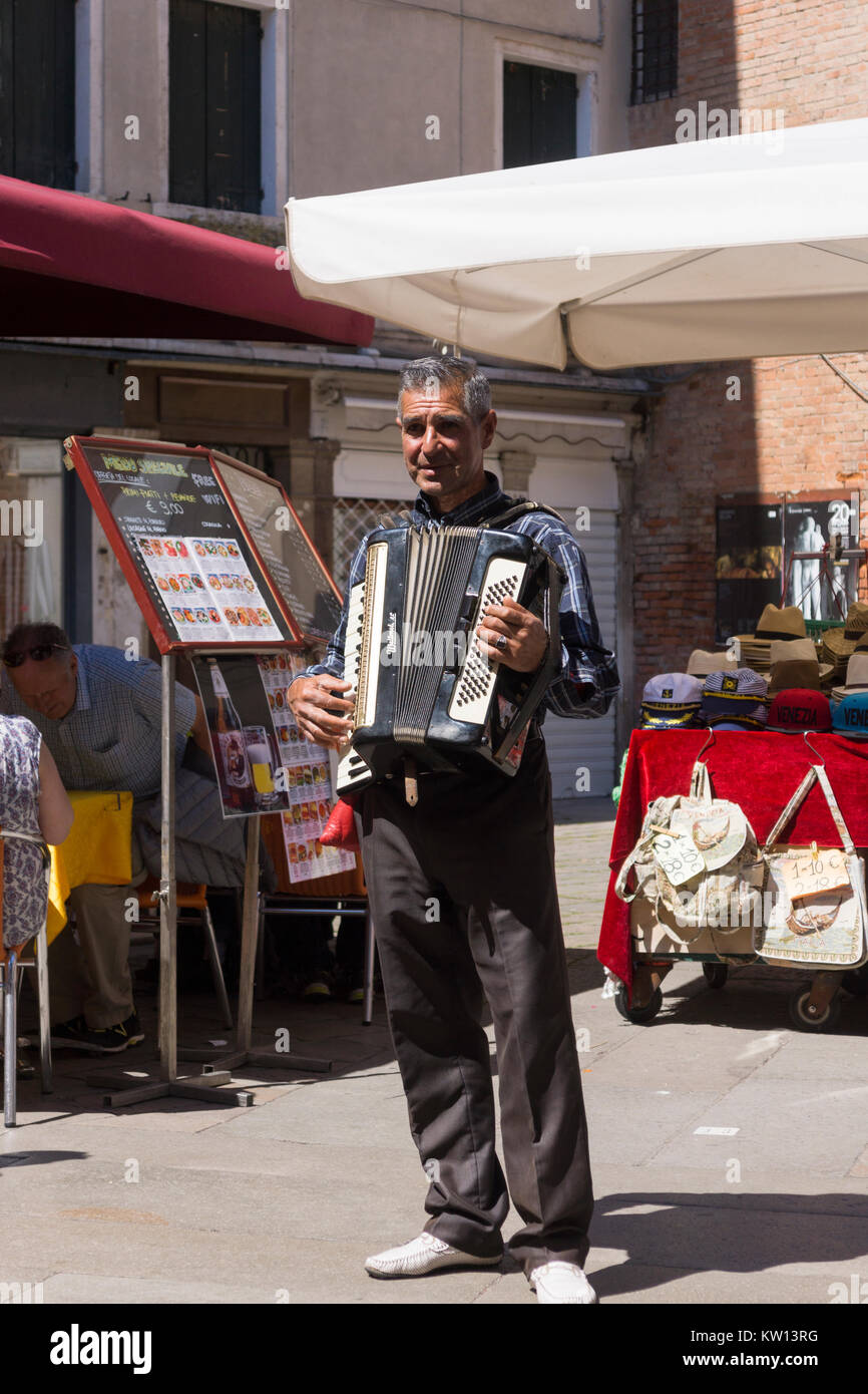 An accordionist playing / busking for diners in a small square in the San Marco quarter of Venice Stock Photo