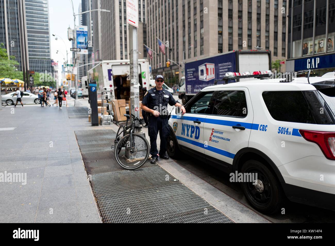 A New York Police Department counter-terrorism officer stands at the ready, while his fellow officer sits in a police vehicle, on 6th Avenue, Manhattan, New York City, New York, July, 2016. Stock Photo