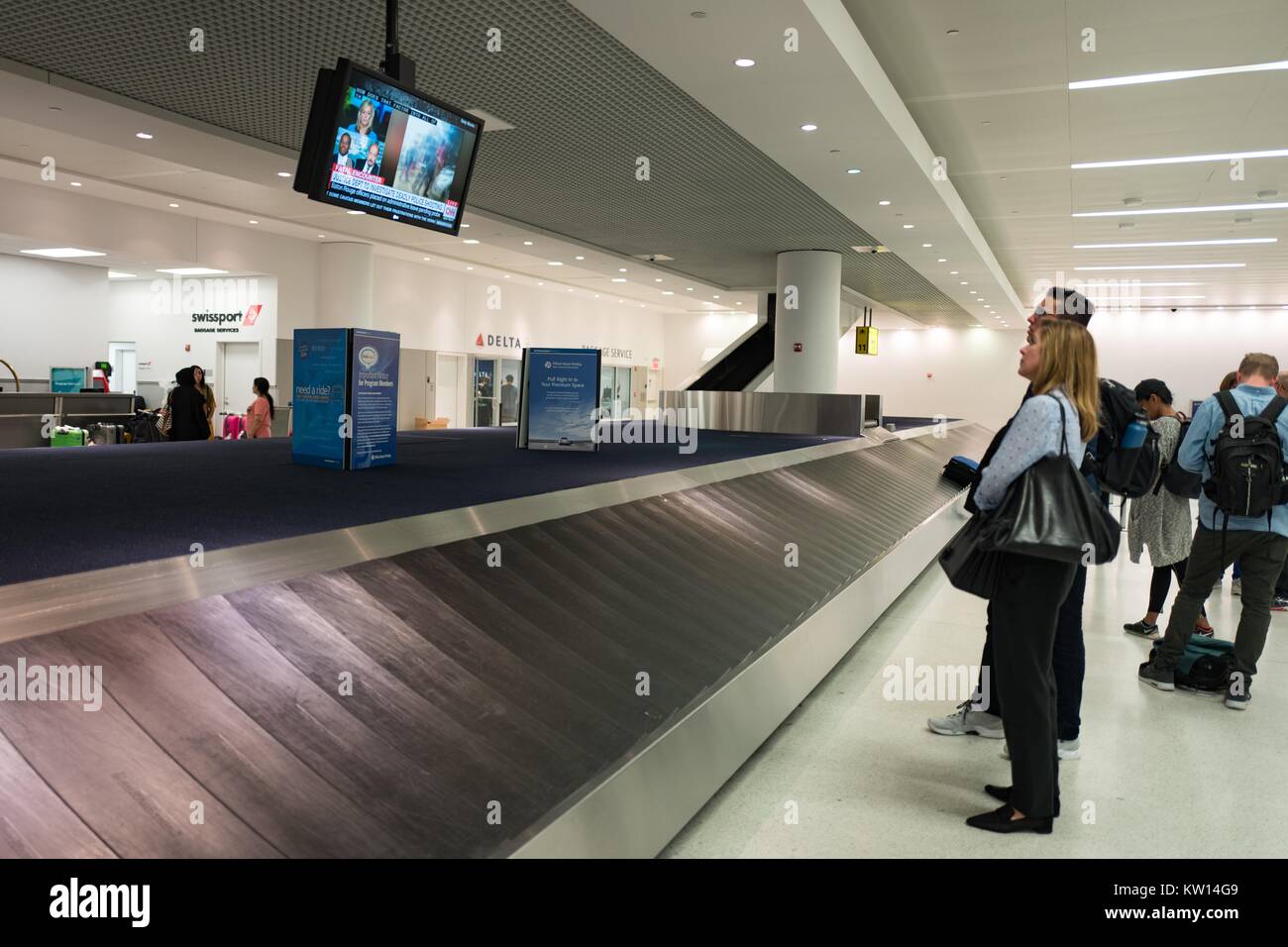 Travelers at Newark International Airport watch a news broadcast about a recent shooting while waiting for their bags to arrive at a baggage carousel, Newark, New Jersey, July, 2016. Stock Photo