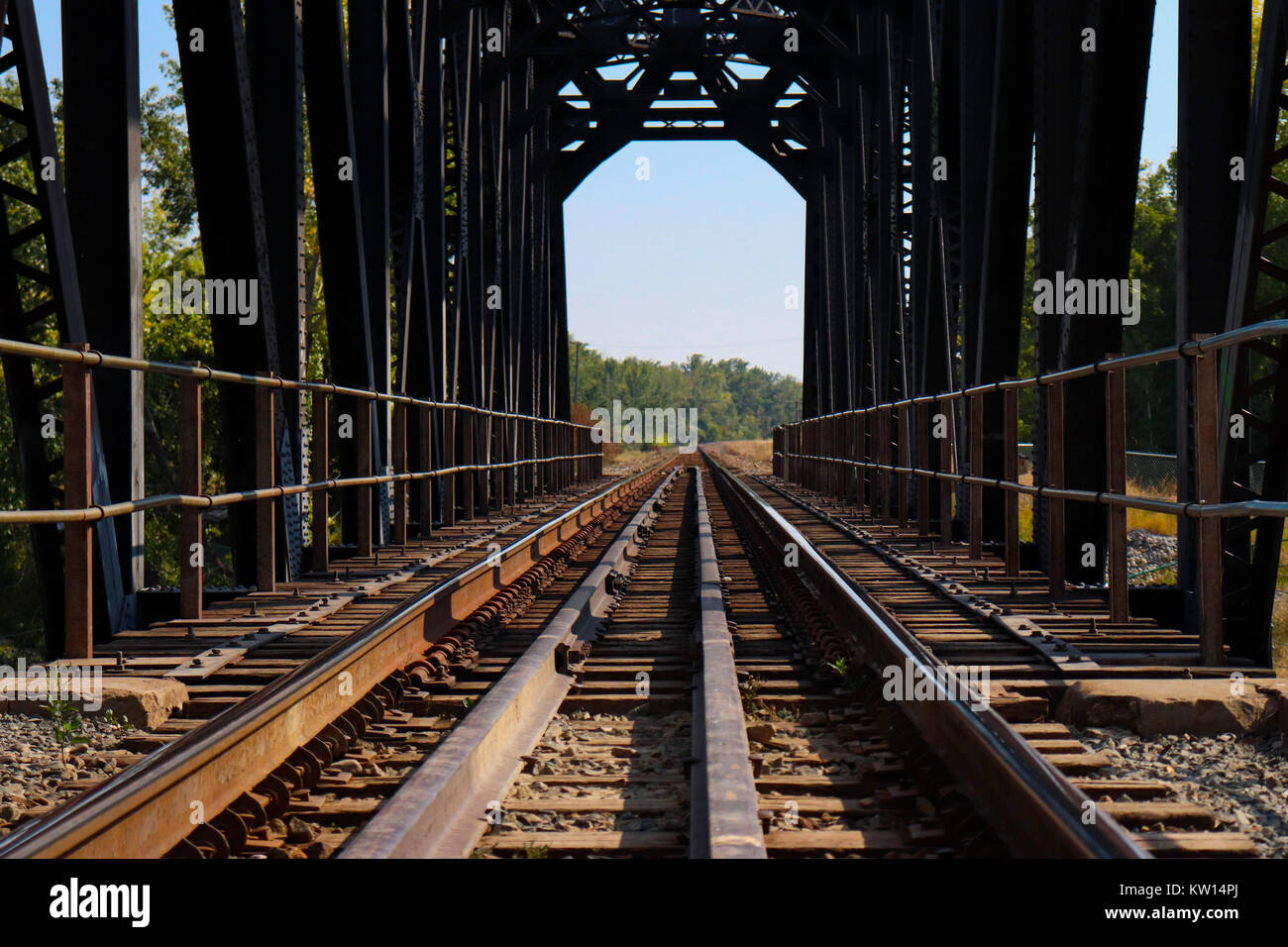 Empty train tracks on a bridge taken from a low angle, blue sky, forest at end Stock Photo