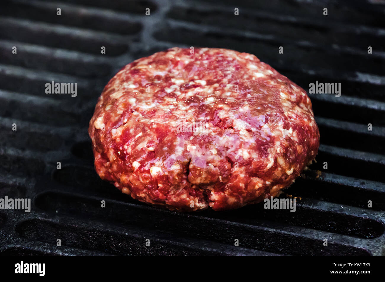 Raw Beef Patty for Burger on black hot grill. Raw Patty of fresh ground