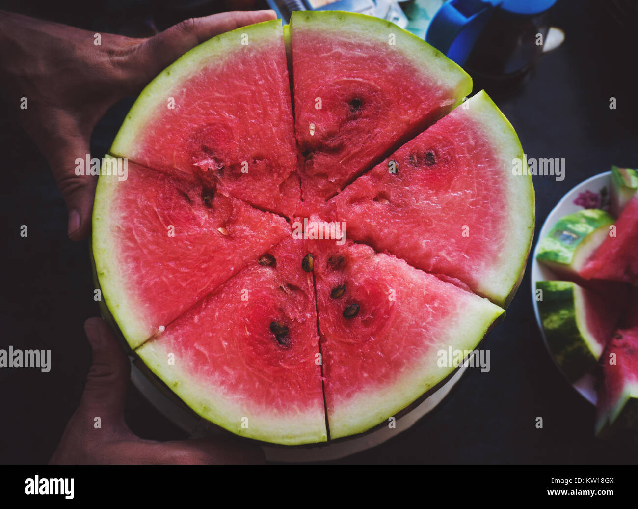 Man cuts red juicy ripe watermelon in slices with knife on dark background slowmotion. Slices of watermelon closeup Stock Photo