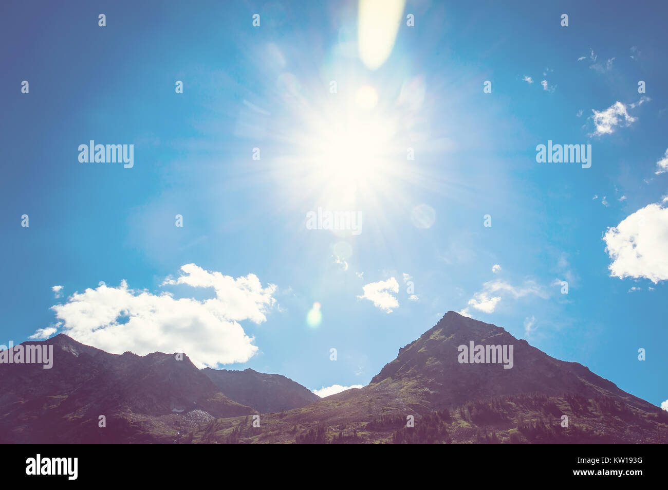 top of mountains in blue sky. The sun shines brightly over the top of a ...