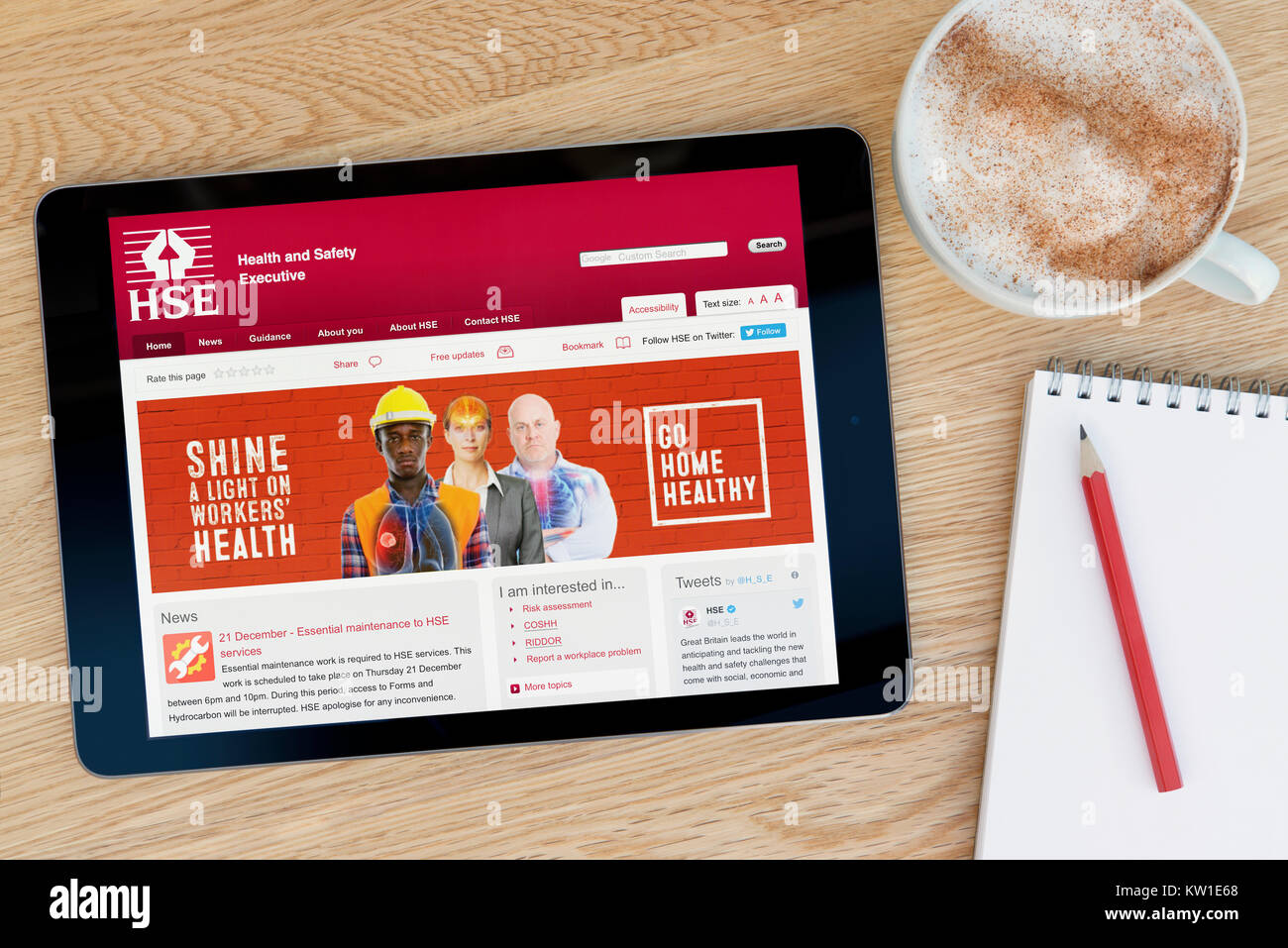 The Health and Safety Executive (HSE) website on an iPad tablet resting on a wooden table beside a notepad, pencil and cup of coffee (Editorial only) Stock Photo