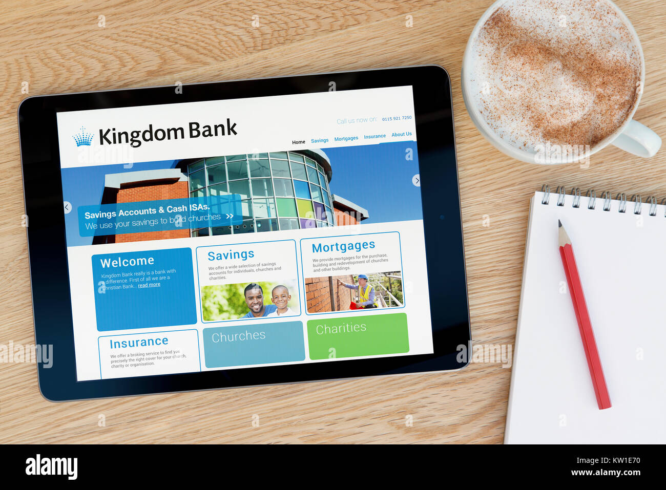 The Kingdom Bank website on an iPad tablet device, resting on a wooden table beside a notepad, pencil and cup of coffee (Editorial only) Stock Photo