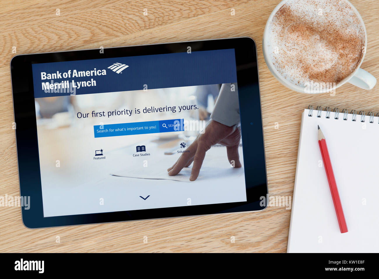 The Merrill Lynch bank website on an iPad tablet device, resting on a wooden table beside a notepad, pencil and cup of coffee (Editorial only) Stock Photo