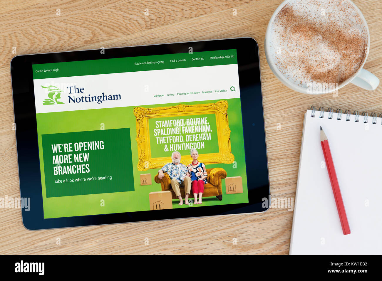 The Nottingham Building Society website on an iPad tablet device, resting on a wooden table beside a notepad, pencil and cup of coffee (Editorial only Stock Photo