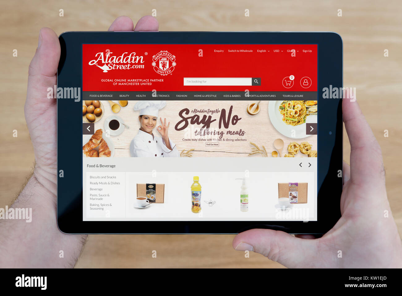 A man looks at the Aladdin Street website on his iPad tablet device, shot against a wooden table top background (Editorial use only) Stock Photo