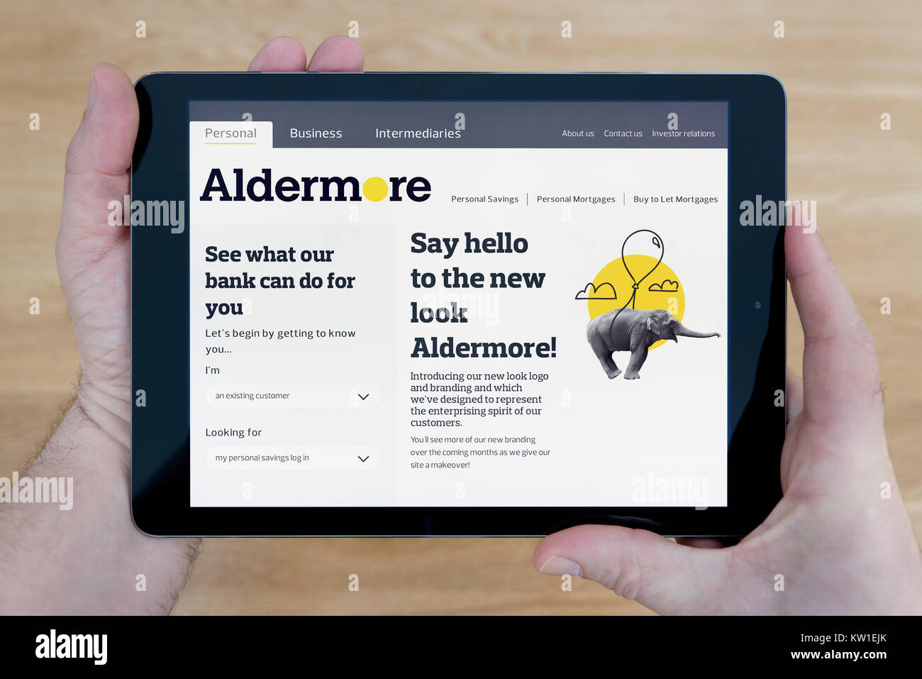 A man looks at the Aldermore Bank website on his iPad tablet device, shot against a wooden table top background (Editorial use only) Stock Photo