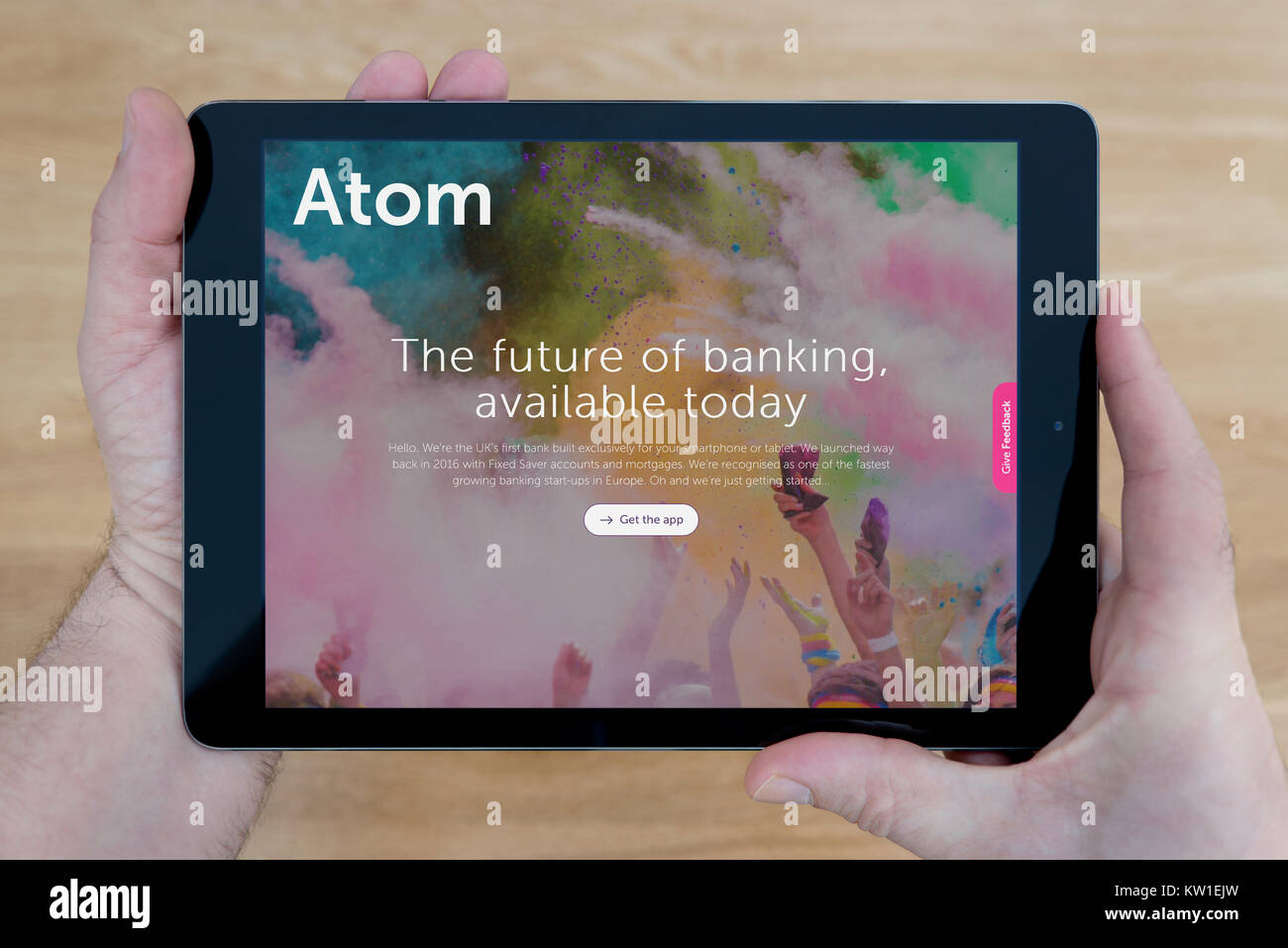 A man looks at the Atom Bank website on his iPad tablet device, shot against a wooden table top background (Editorial use only) Stock Photo